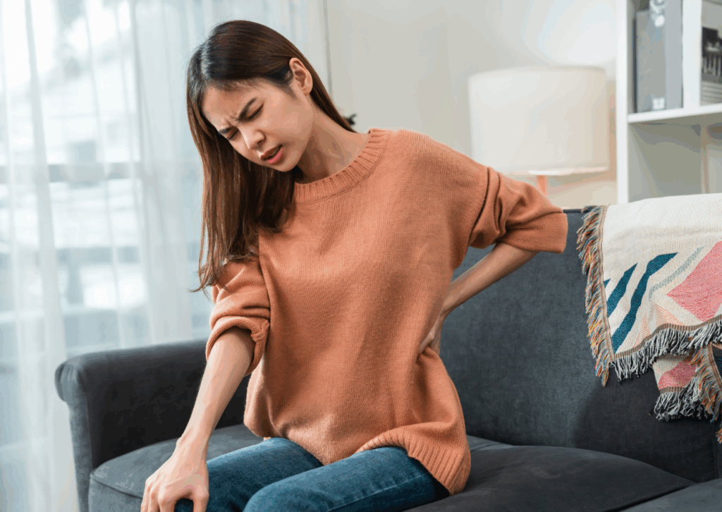 Donna seduta sul divano con espressione di dolore lombare, possibile sintomo di fibromialgia. Esempio di dolore cronico trattabile con Limfa® Therapy alla FisioClinic del Centro Colombo Genova.